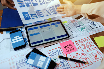 Close up ux developer and ui designer brainstorming about mobile app interface wireframe design on table with customer breif and color code at modern office.Creative digital development agency.