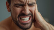 © Iwan Rusly - young man suffering from severe toothache, holding his cheek in pain and grimacing with closed eyes. Concept of dental pain, tooth decay, or jaw problem.
