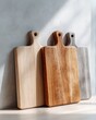 Three wooden cutting boards are stacked together on a light surface, highlighting their various colors and natural grain patterns. Soft light enhances their beauty.