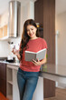 © Fahng - Beautiful young woman sitting at kitchen counter in the morning, drinking fresh water and reading a book, relaxing and enjoying her leisure time at home.