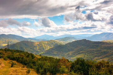 Wall Mural - autumn landscape in mountains. beautiful view of countryside in europe. colorful carpathian alps of ukraine in the background. cloudy sky. picturesque rural scenery with village in the valley