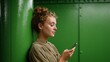 © iuricazac - Woman using cell phone against green wall in urban setting.