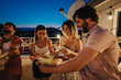© qunica.com - A group of friends shares a joyous rooftop moment, enjoying melon slices and live music as the sun sets, creating a warm and cheerful evening atmosphere filled with bonding and lively conversation.
