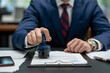 © Din Nasahrudin - A corporate worker applying a stamp to an official document in the office, showcasing the business process of document approval and paperwork handling