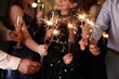 © New Africa - Friends celebrating New Year with sparklers and wine glasses indoors, closeup