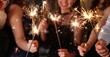 © New Africa - Friends celebrating New Year with sparklers and wine glasses indoors, closeup