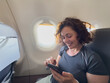© Юлия Завалишина - Passenger woman is flying in plane. Girl using phone sitting by airplane window. Traveling female with smartphone inside plane enjoying flight. Woman using wifi connection on board. Traveling girl