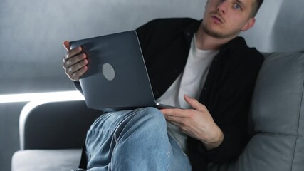 A young IT specialist sitting on a gray sofa with a laptop finishes working and closes the laptop.
A tired IT specialist closes the laptop.
End of the workday.
Laptop, IT, work, tired