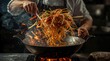 © ACE STEEL D - Chef tossing stir fry noodles dramatically in a fiery hot wok