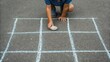 © nunoi - A child drawing a tic-tac-toe grid on asphalt with chalk, preparing for a game.