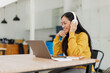 © David - Asian Woman Student Studying in a Traditional Library. Wearing Headphones, Working on an University Research Project, Reading Academic Textbook and Journals Online