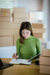 © Witoon - A young female entrepreneur managing online orders, packing parcels, and running a small e-commerce business with professionalism and happiness.