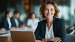 © Kateryna - Portrait of self assured confident businesswoman with laptop at conference table sitting in modern boardroom while colleagues collaborate productively in background professional