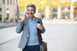 © Miquel - Happy businessman walking city street making phone call