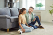 © Studio Romantic - Happy conversation of couple looking to each other with love, dialogue of people sitting at sofa on floor in home living room. Man holding smartphone, smiling to woman. Romantic relationship concept
