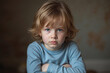 © Aleksei Solovev - A young child with long blonde hair and blue eyes, wearing a blue shirt, sitting with crossed arms.