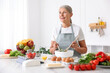 © New Africa - Senior woman cooking salad at white marble table in kitchen