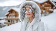 © Sergey - Model in luxury white ski outfit with fur hood and reflective sunglasses, standing on snowy mountain slope with alpine chalets in background