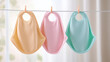© kora studio - Colorful baby bibs hanging on clothesline, pastel shades of yellow, pink, and blue. soft fabric and playful design make them perfect for mealtime