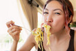 © EdNurg - Young woman is very hungry and greedily eating spaghetti with a fork from plate in a restaurant
