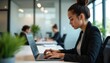 © miss irine - Woman works on laptop in office. She wears blazer. Lady sits at desk, types on keyboard. Colleagues at background. Concept of work at tech company coding.