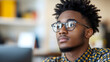 © VinakMotion - Young man with glasses in a thoughtful pose, sitting in a modern office environment with blurred background elements
