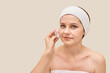 © elenavolf - Female adult caucasian beauty skincare routine with cotton pad and headband on beige background.