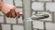 © Feliks - A hand holds a trowel with wet cement mixture over a blurry background of a light-colored brick wall
