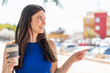 © luismolinero - Young pretty Brazilian woman holding a take away coffee at outdoors pointing to the side to present a product
