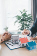 © doidam10 - Close up of real estate agent showing small house model to client with calculator, contract paperwork on desk, concept of mortgage loan, home ownership, property investment agreement. mortgage loan