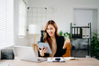 © Nuttapong punna - Asian businesswoman celebrating success in modern office, holding tablet and smiling with laptop, showing joy and achievement in work, startup, and digital business.