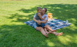 © Ekaterina - Mother tenderly hugs her autistic son while sitting on a picnic blanket in green park, enjoying beautiful sunny summer day with a teddy bear and drinks next to them