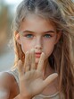 © Eakanan - A young girl with striking blue eyes and freckles holds her sand covered hand up in a stop gesture against a soft natural background