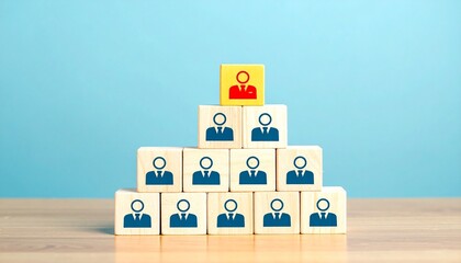 Wooden block pyramid with blue icons and one yellow leader block on light blue background.