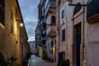 © Tomasz - Blue-Hour Alley with Traditional Balconies, Warm Lanterns and Textured Limestone