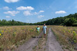 © Ekaterina - Senior couple walking along a dirt road, surrounded by a sunny sunflower field under a clear blue sky, experiencing active retirement and enjoying life outdoors during summer
