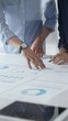© rogerphoto - Business people are examining financial data, pointing at charts and graphs spread out on a table during a collaborative analysis session in a modern office, close up vertical view