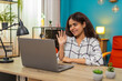 © Andrii Iemelianenko - Indian woman at home joins video call waves hand and smiles welcoming friend through laptop screen. Arabian girl at table speaks lively making eye contact building warm connection with webcam on desk.