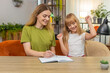 © Andrii Iemelianenko - Mother and daughter at home draw grid on paper play tic tac toe fast rounds keep score in notebook. Woman and girl at table mark cross and noughts laugh plan rematch cheer friendly match track points.