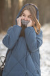 © shymar27 - Young woman wearing a blue quilted jacket stands outdoors in a snowy landscape, surrounded by trees, showcasing winter fashion and serene nature vibes