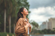 © oatawa - Carefree asian woman standing in city park enjoying fresh air and nature – happy female smiling and breathing deeply in urban green space, mindful wellness lifestyle and outdoor relaxation