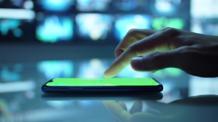 Close-up of a hand interacting with a smartphone screen displaying a vibrant green interface in a tech setting