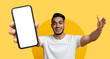 © Prostock-studio - A joyful man is standing with outstretched arms, presenting a smartphone. He is smiling widely, set against a vibrant yellow background, conveying a sense of excitement and engagement.