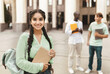 © Prostock-studio - Loans for education concept. Portrait of happy indian female student smiling at camera while posing outdoors in campus with her classmates and university building on background