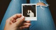 © Hungarian - A hand holding a faded vintage photograph displays two figures, the aged Polaroid picture resting against a person's torn blue jeans, creating a nostalgic memory moment and visual storytelling.
