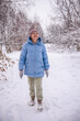 © StockMediaSeller - Elderly woman in a blue winter coat walking through a snowy forest path and looking up at the falling snow. She enjoys the beauty and calmness of nature on a quiet winter day.