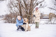 © StockMediaSeller - Elderly woman and her adult daughter enjoying a winter walk with their Golden Retriever. The daughter kneels to pet the happy dog while the mother holds the leash, surrounded by snowy trees