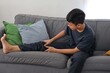 © Gatot - Asian Child Boy Stretching Leg Muscles on Sofa While Massaging from Cramp