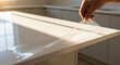 © MT - Close-up of a person's hand carefully peeling off a clear protective film from a new white kitchen countertop, revealing its pristine surface in a modern home interior.