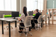 © Богдан Маліцький - African American woman and European young man in business suit sitting in office and typing on computer, office workers working online and looking at monitor, back view